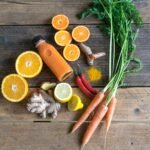 Fresh immune-boosting foods including ginger, turmeric, carrots and citrus fruits on a wooden surface