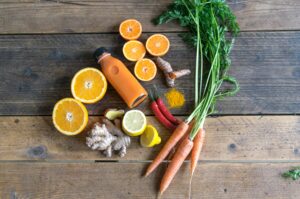 Fresh immune-boosting foods including ginger, turmeric, carrots and citrus fruits on a wooden surface